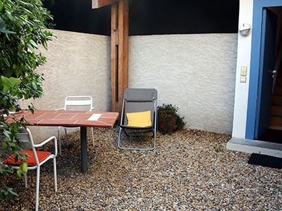 Coin détente en terrasse avec table en terre cuite, chaises blanches et fauteuil de jardin sur sol en gravier.