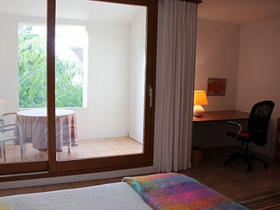 Chambre avec bureau et baie vitrée ouvrant sur une terrasse privée avec table ronde et chaises.