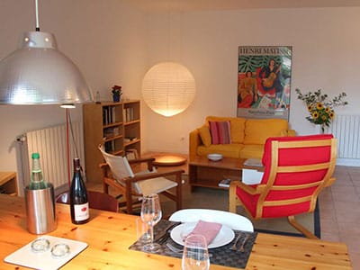 Salon chaleureux avec canapé jaune, fauteuil rouge, table dressée et affiche Henri Matisse sous des luminaires design.