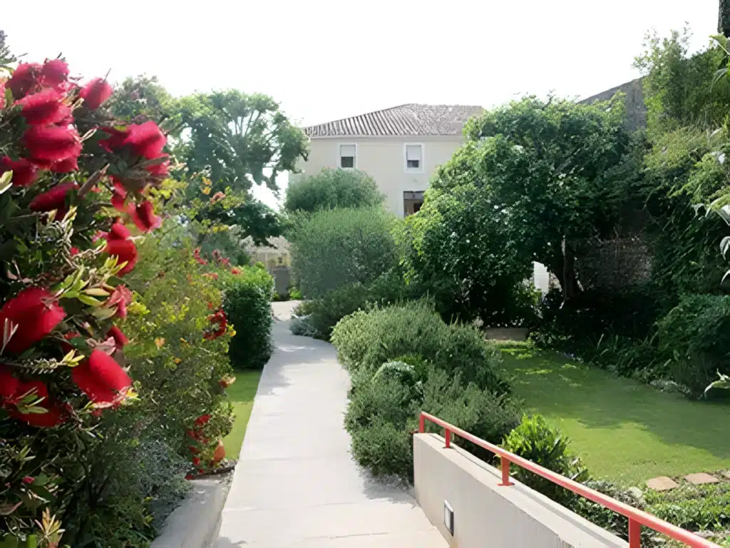 Jardin paysager avec sentier et fleurs rouges éclatantes Sentier de jardin avec fleurs rince-bouteille rouges menant vers une maison entourée de verdure luxuriante.