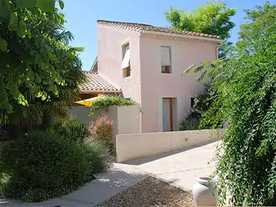 Maison rose méditerranéenne au toit de tuiles entourée d'un jardin verdoyant et luxuriant.