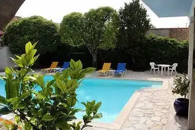 Piscine avec Jardin et Terrasse pour Détente Estivale Piscine bleu clair avec chaises longues, terrasse en pierre et jardin arboré pour un espace de détente estival.