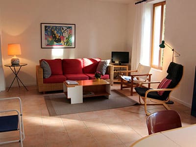 Salon chaleureux avec canapé rouge, fauteuil noir, table basse bois et déco colorée baignée de lumière naturelle.