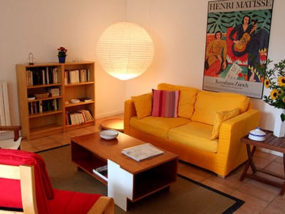 Salon chaleureux avec canapé jaune, affiche Henri Matisse, lampe sphérique et bibliothèque en bois.