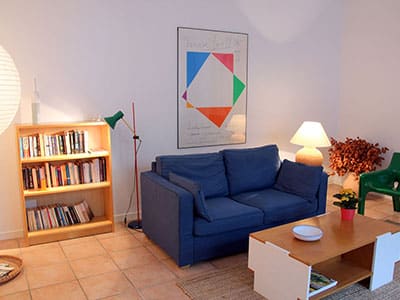 Canapé bleu, bibliothèque en bois et affiche géométrique Max Bill dans un salon moderne chaleureux.