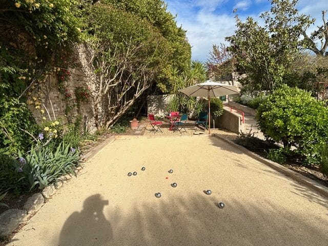 Terrain de Pétanque et Jardin : Détente et Loisirs Extérieurs Terrain de pétanque ensoleillé dans un jardin fleuri avec boules sur le sable et coin détente sous un parasol.