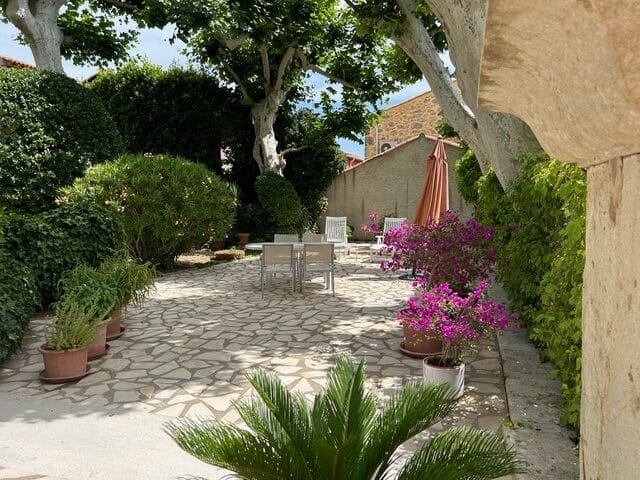 Terrasse méditerranéenne avec mobilier et bougainvilliers Terrasse en pierre avec mobilier blanc, bougainvilliers en fleurs et parasol dans un jardin ombragé paisible.